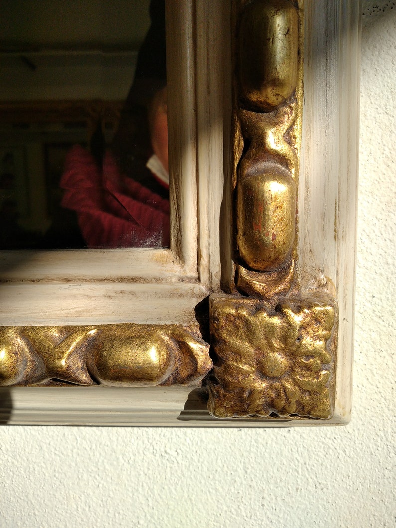 May include: A close-up of a white and gold ornate picture frame. The frame has a decorative design with gold accents and a white background.