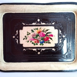 May include: A vintage metal tray with a black background and a white border. The tray features an ornate design and a painted floral motif in the center.