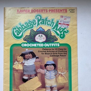 Könnte beinhalten: Ein Häkelmusterbuch für Cabbage Patch Kids Puppen. Der Umschlag zeigt zwei Puppen in gehäkelten Outfits und einen Titel, der "Crocheted Outfits" lautet. Das Buch enthält Muster für 20 einfach zu häkelnde Kleidungsstücke für Jungen und Mädchen.