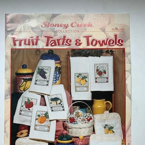 May include: A book titled "Fruit Tarts & Towels" from the Stoney Creek Collection. The book cover features a colourful display of kitchen towels with embroidered fruit designs, including apples, oranges, strawberries, lemons, and grapes. The book is priced at £5.50.