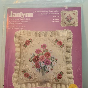 May include: A white pillow with a floral embroidery design. The embroidery features pink and white flowers with green leaves. The pillow is surrounded by a white lace trim. The packaging includes instructions for the embroidery project. The text on the packaging reads "Candlewicking Embroidery #04-758 Cosmos Le Cosmos".