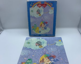 May include: A Care Bears jigsaw puzzle with 60 pieces. The puzzle features the Care Bears on clouds with a rainbow and hearts. The puzzle is made by Elma.