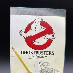 May include: A Ghostbusters movie scrapbook with a red no ghost symbol and a drawing of the Stay Puft Marshmallow Man. The cover has the text "Ghostbusters Movie Scrapbook" and "Stay Puft Marshmallow Man attacks New York".