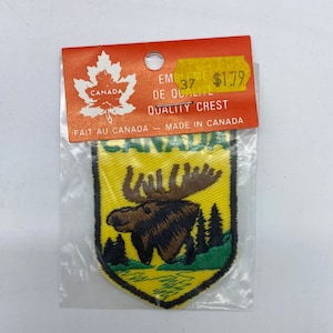 以下が含まれることがあります： 黄色と緑色の刺繍が施されたパッチで、ヘラジカと「CANADA」の文字が盾の形にデザインされています。パッチは透明なビニール袋に入っていて、赤と黄色の値札には「$1.79」と表示されています。