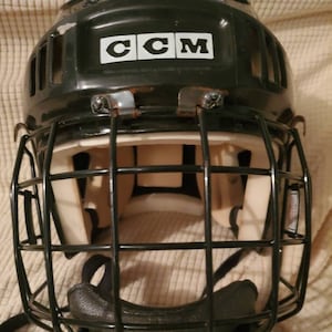 Peut inclure: Casque de hockey noir avec une cage noire et un logo CCM blanc à l'avant.