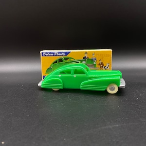 Può includere: Un'auto giocattolo di plastica verde con una scatola su cui è scritto "Deluxe Plastic". L'auto ha un interno bianco e ruote argentate.
