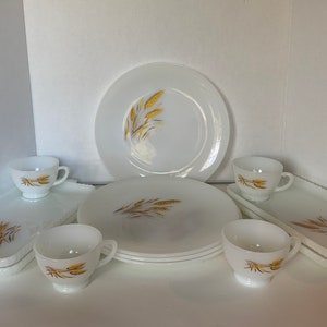 Peut inclure: Un ensemble de vaisselle en verre de lait blanc avec un motif de blé en or. L'ensemble comprend une assiette à dîner, une assiette à salade, une tasse et une soucoupe. Il y a aussi deux plats de service rectangulaires.