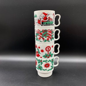 May include: A set of four white ceramic mugs with Christmas-themed designs. The mugs are stacked on top of each other. The designs include Santa Claus, bells, candles, and holly.