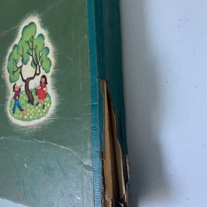 Puede incluir: Un libro antiguo de tapa dura verde con una ilustraci&oacute;n colorida de dos ni&ntilde;os jugando bajo un &aacute;rbol en la portada. El libro est&aacute; ligeramente da&ntilde;ado en el lomo.