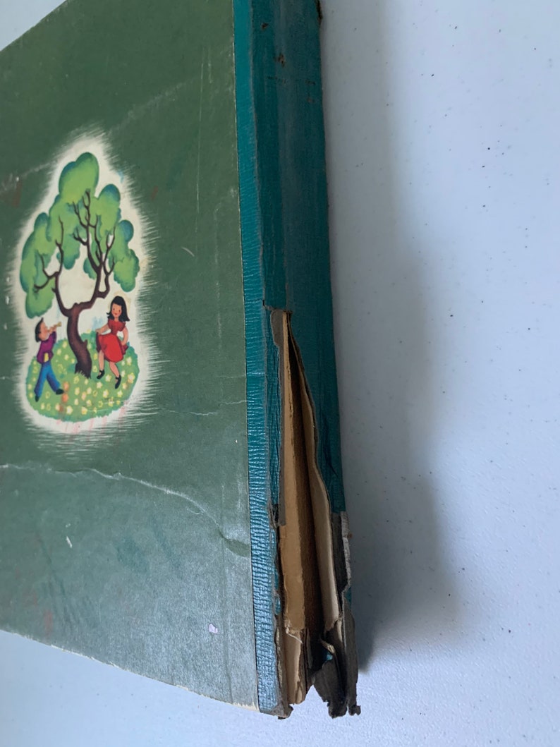 Puede incluir: Un libro antiguo de tapa dura verde con una ilustraci&oacute;n colorida de dos ni&ntilde;os jugando bajo un &aacute;rbol en la portada. El libro est&aacute; ligeramente da&ntilde;ado en el lomo.
