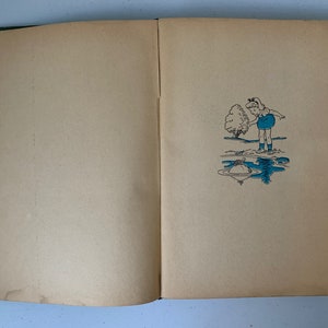 Puede incluir: Un libro abierto con una cubierta verde. La p&aacute;gina derecha tiene una ilustraci&oacute;n en blanco y negro de una ni&ntilde;a con un vestido azul de pie junto a un charco de agua. Una peque&ntilde;a tortuga est&aacute; en el charco.