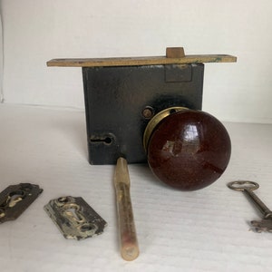 Peut inclure: Une poignée de porte antique avec un bouton en céramique marron, un trou de serrure en laiton et une clé en laiton. Le bouton est fixé à une serrure de porte en métal noir avec une plaque en laiton.