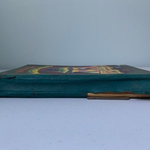 Puede incluir: Un libro antiguo de tapa dura verde con una ilustraci&oacute;n colorida en la portada. El libro est&aacute; ligeramente desgastado y tiene un desgarro en el borde inferior.