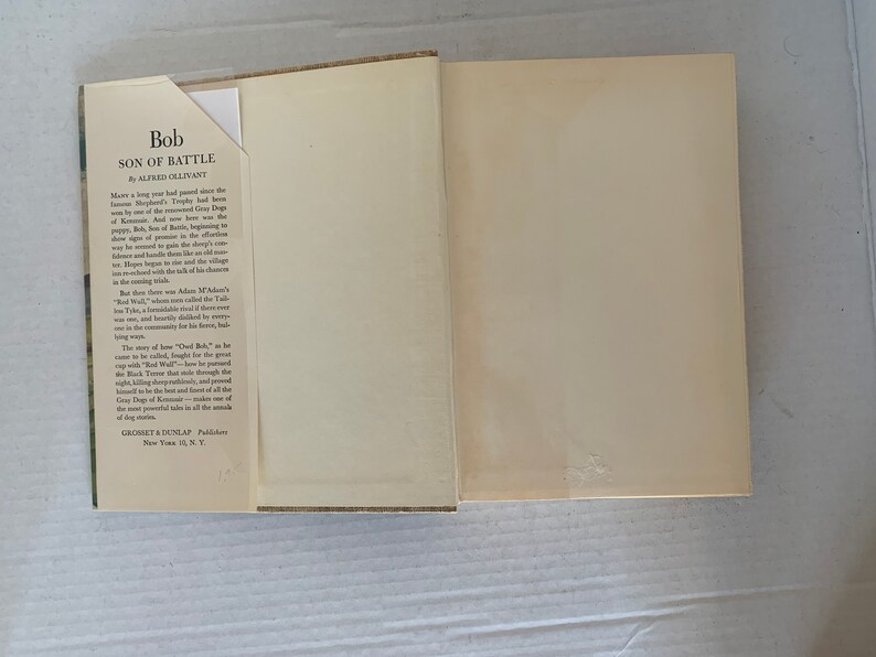 May include: A vintage book titled "Bob, Son of Battle" by Alfred Ollivant. The book cover features a brown and green illustration of a dog in a forest setting. The book is published by Grosset & Dunlap, New York 13, N.Y.