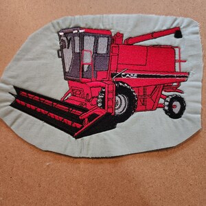 May include: Embroidered patch depicting a red Case combine harvester. The patch is set against a pale green backdrop. The combine features black and silver details, including the wheels and the Case logo. The patch is likely for a jacket or bag.