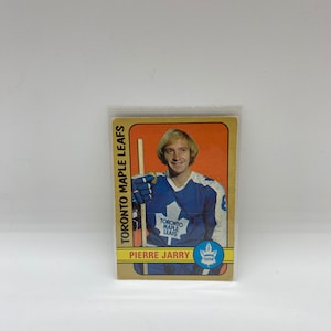 May include: A vintage hockey card featuring Pierre Jarry of the Toronto Maple Leafs. The card has a yellow background with a blue and white team logo. The card is in a plastic protective sleeve.
