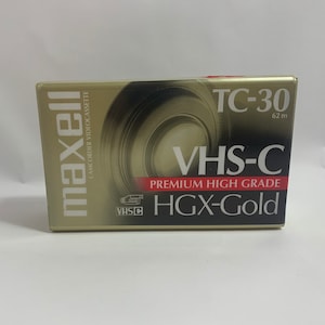 May include: A gold Maxell VHS-C video cassette with the text "TC-30 62 m" and "VHS-C PREMIUM HIGH GRADE HGX-Gold" printed on the label.