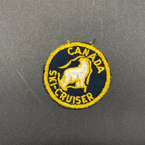 May include: A yellow and blue embroidered patch with a white goat and the text "CANADA SKI-CRUISER".