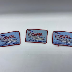 Könnte beinhalten: Drei blaue und rote gestickte Aufnäher mit dem Text "Air Jew-Bec" und dem Ort "Bathurst, N.B. Canada". Jeder Aufnäher zeigt eine kleine Flugzeuggrafik.