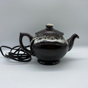 Puede incluir: Una tetera eléctrica de cerámica marrón y blanca con un cable.