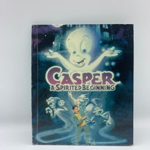 以下が含まれることがあります： アニメキャラクターのフレンドリーな幽霊カスペルをフィーチャーしたDVDケース。カバーアートは、カスペルが少年と他の幽霊と一緒に、不気味な設定で描かれています。タイトル「カスペル：スピリテッド・ビギニング」は、黒地に白で印刷されています。