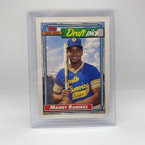 May include: A Topps Major League baseball card featuring Manny Ramirez, a baseball player wearing a blue and yellow uniform with the text "South Service League" on the front. The card is a draft pick card with a green and white "Draft Pick" banner.