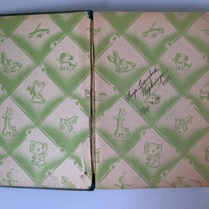 Puede incluir: Un libro infantil vintage con una cubierta de patr&oacute;n verde y blanco. La cubierta presenta una variedad de juguetes, incluyendo una jirafa, un caballo de balanc&iacute;n, un tambor y un tren de juguete. El libro est&aacute; inscrito con el nombre "Hope Laughlin" y la fecha "5 de mayo de 1948".
