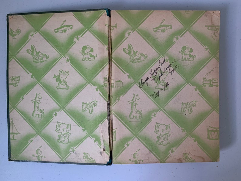 Puede incluir: Un libro infantil vintage con una cubierta de patr&oacute;n verde y blanco. La cubierta presenta una variedad de juguetes, incluyendo una jirafa, un caballo de balanc&iacute;n, un tambor y un tren de juguete. El libro est&aacute; inscrito con el nombre "Hope Laughlin" y la fecha "5 de mayo de 1948".