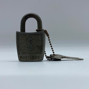Puede incluir: Un candado plateado con una llave unida a una cadena. El candado tiene una letra "S" en la parte delantera y la palabra "RUSTLESS" impresa debajo.