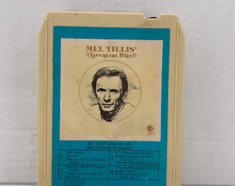 Può includere: Un nastro audio vintage con un ritratto del cantante di musica country Mel Tillis. Il nastro è intitolato "Mel Tillis Greatest Hits" e presenta un elenco di canzoni sul retro. Il nastro è in una custodia di plastica bianca con un bordo blu.
