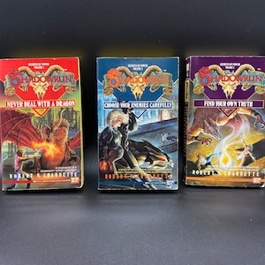 May include: Three paperback fantasy novels with colorful covers featuring dragons, a woman with a sword, and a wolf. The titles are "Never Deal with a Dragon", "Choose Your Enemies Carefully", and "Find Your Own Truth".