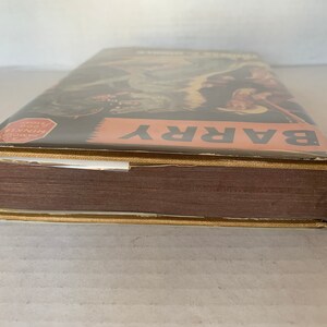 May include: A brown hardback book with a gold spine and a dust jacket. The dust jacket features a colourful illustration of a cowboy riding a horse. The text "BARRY" is printed in large white letters on the dust jacket. The text "HISTORY OF THE WORLD" is printed in red on a white circle on the dust jacket.