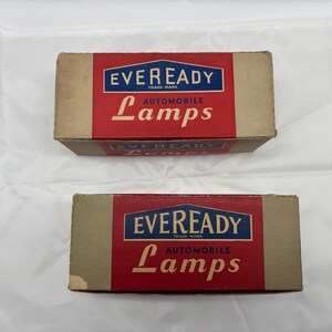 May include: Two vintage Eveready Automobile Lamps boxes. Each box has a red and blue label with the brand name and product description. The boxes are rectangular with a tan cardboard exterior.