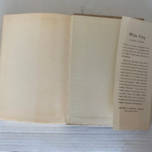 May include: A white book with the title "White Fang" by Jack London on the spine. The book is open to the inside cover, which has a description of the book.
