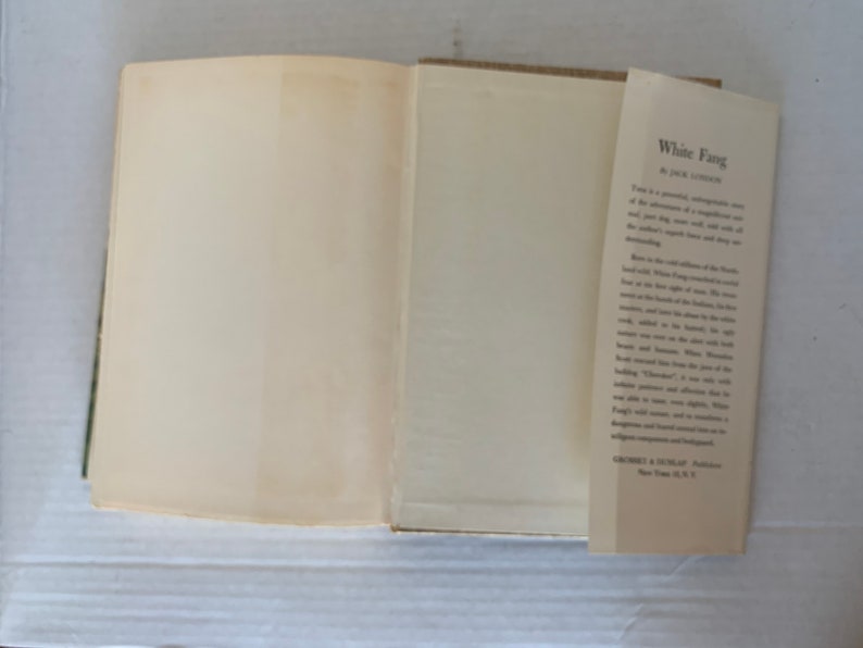 May include: A white book with the title "White Fang" by Jack London on the spine. The book is open to the inside cover, which has a description of the book.