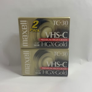 May include: Two-pack of Maxell VHS-C video cassette tapes. Each tape is gold and black with the text "TC-30 62m VHS-C PREMIUM HIGH GRADE HGX-Gold" printed on the label.