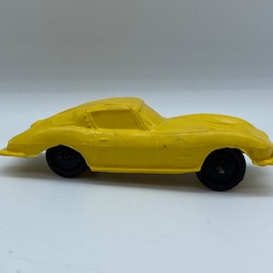 May include: A yellow plastic toy car with black wheels. The car is a vintage model and has a classic sports car design.