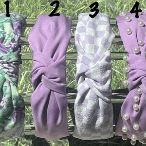 May include: Four purple headbands with different designs. The first headband has a floral pattern, the second is solid purple, the third has a checkered pattern, and the fourth has pearl embellishments.