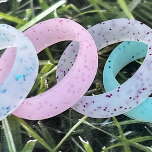 May include: Four silicone rings with glitter embedded in the silicone. The rings are in the colors white, pink, light blue, and a darker blue.