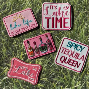 Puede incluir: Parches bordados rosas y blancos con temas de lago y tequila. Uno dice "Lake Life is the Best Life", otro "It's Lake Time" y un tercero "Spicy Tequila Queen".