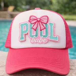 May include: A pink and white trucker hat with the words "POOL babe" in teal and pink. The hat features a pink bow and a mesh back. The brim and the top of the hat are pink.
