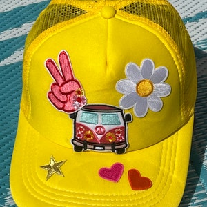 May include: Yellow trucker hat with a peace sign, a daisy, a van with a peace sign, a star, and two hearts.