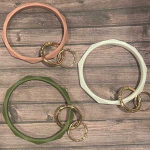 May include: Three silicone keychains in pink, white, and green. Each keychain has a gold metal ring attached.