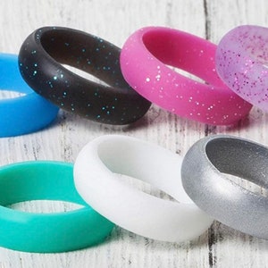 May include: Assortment of silicone rings in various colors, including blue, black, pink, purple, teal, white, and silver. Some rings have glitter embedded in the silicone.