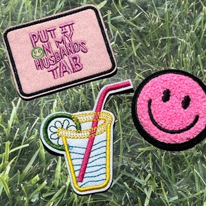 Può includere: Tre toppe ricamate da stirare. Una toppa rosa con il testo "PUT IT ON MY HUSBANDS TAB". Una toppa con un'emoticon sorridente rosa. Una toppa gialla e verde con un bicchiere di limonata con una cannuccia rosa.