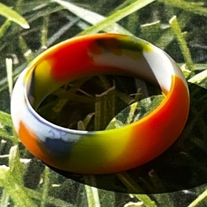 May include: A colorful silicone ring with a camouflage pattern in shades of orange, yellow, white, and blue.