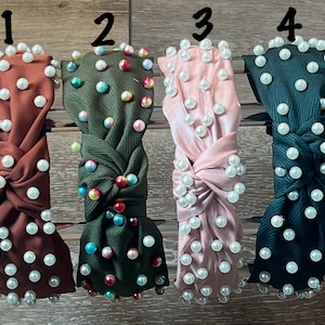 May include: Four different styles of knotted headbands with pearl embellishments. The headbands are in brown, green, pink, and dark green.