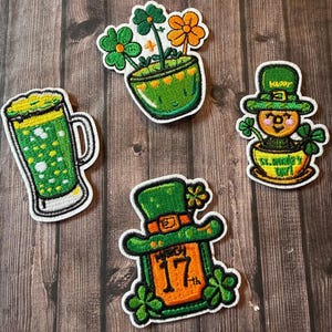 Peut inclure: Quatre écussons brodés sur le thème de la Saint-Patrick. L'un est un mug de bière verte, un autre est un pot vert avec des fleurs, un troisième est un lutin dans une tasse et le dernier est un chapeau vert avec la date du 17 mars.