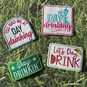 Puede incluir: Cuatro parches bordados con frases relacionadas con el consumo de alcohol durante el día. Los parches son blancos, verdes y rosas, con textos como "Day Drinking" y "Let's Day Drink". Los parches están sobre hierba verde.