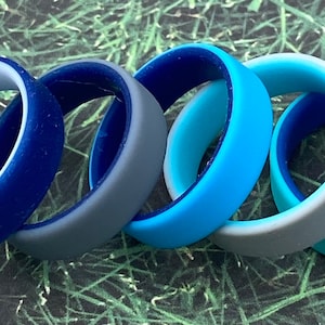 Puede incluir: Cinco anillos de silicona en varios tonos de azul. Los anillos están apilados uno encima del otro, con el anillo azul más oscuro en la parte inferior y el anillo azul más claro en la parte superior.